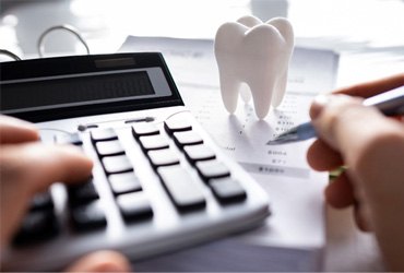 Person typing on calculator with model of tooth on desk