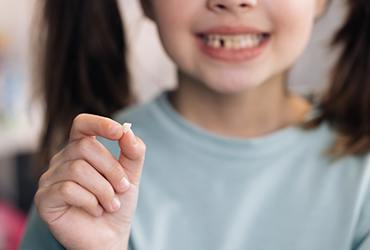 Smiling child holding her extracted tooth